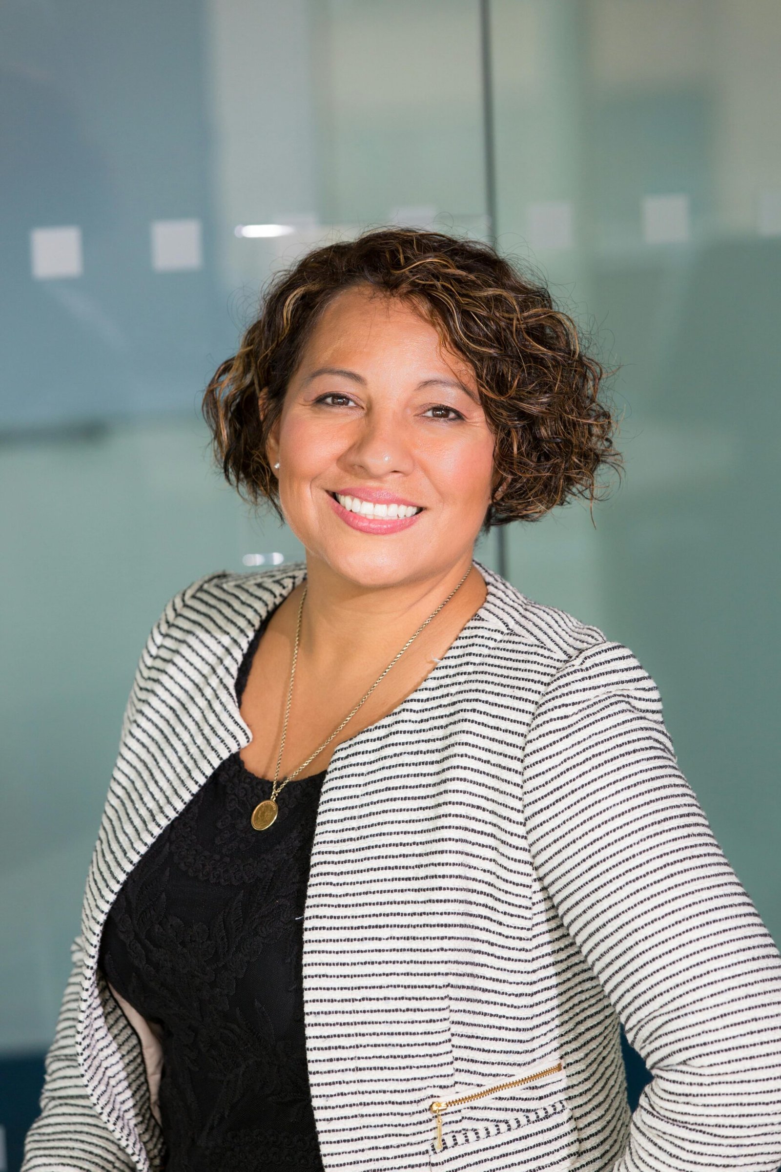 A confident woman with curly hair smiling in an office environment, conveying professionalism and approachability.